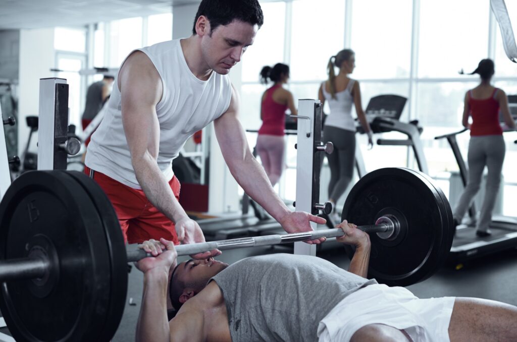 person spotting friend as he performs bench press using heavy weights